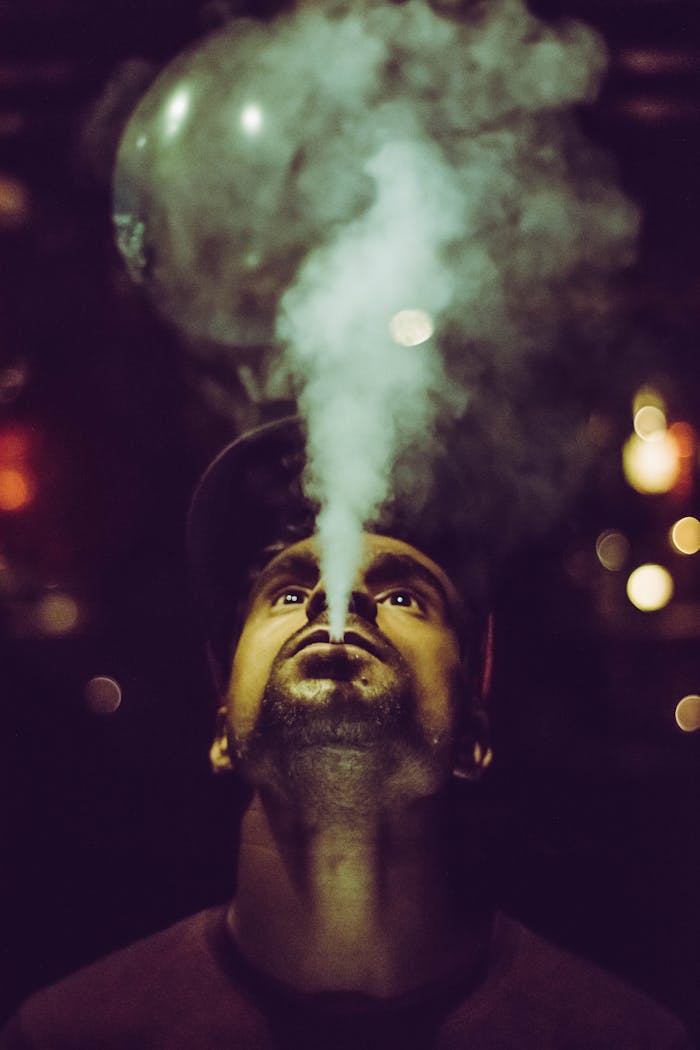 Low-angle portrait of a man vaping at night with artistic bokeh effects in the background.