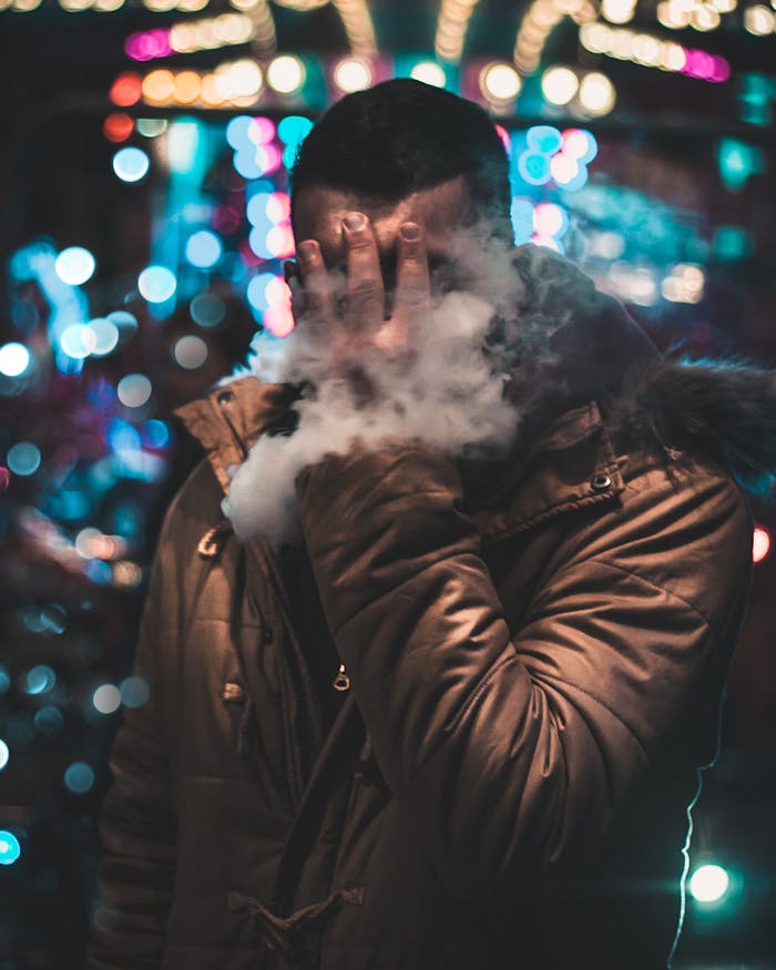Man vaping at night with colorful bokeh lights in Dumfries, Scotland.