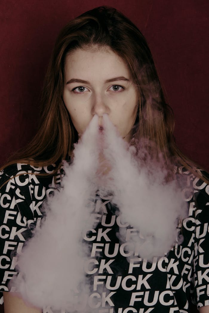 our-story-02 Portrait of a young woman vaping indoors, creating a dramatic smoke effect.